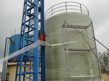 A vertical filament winding machine is winding structural layers of FRP tanks.